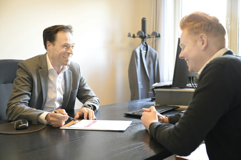 Two smiling men discussing documents across an office desk