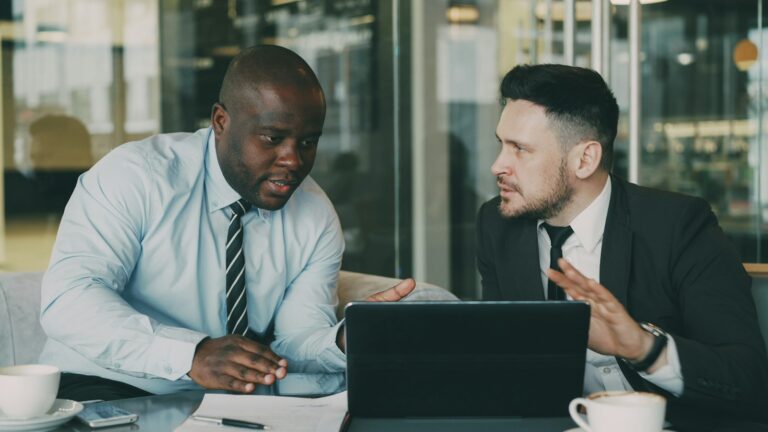 Two colleagues collaborating over a tablet and laptop