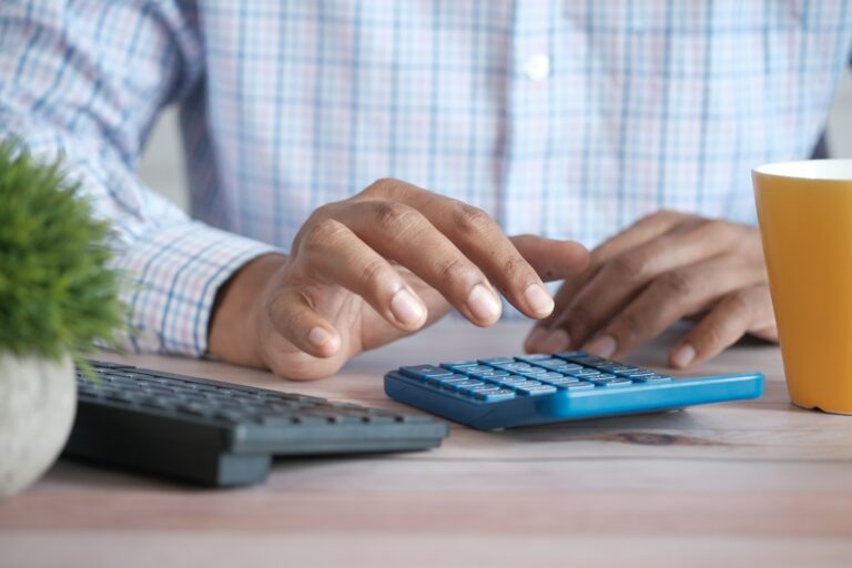 Hand using a calculator on a desk while reviewing costs